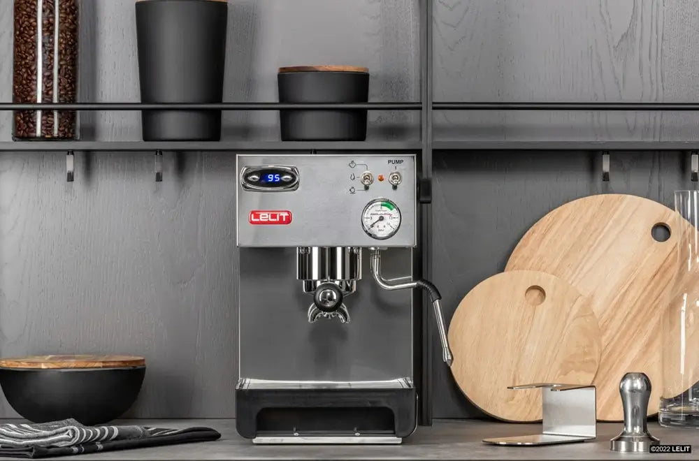 A stainless steel Lelit Anna espresso machine positioned on a modern gray kitchen counter. The machine features a digital temperature display reading "95," a round analog pressure gauge, and toggle switches on the front panel.