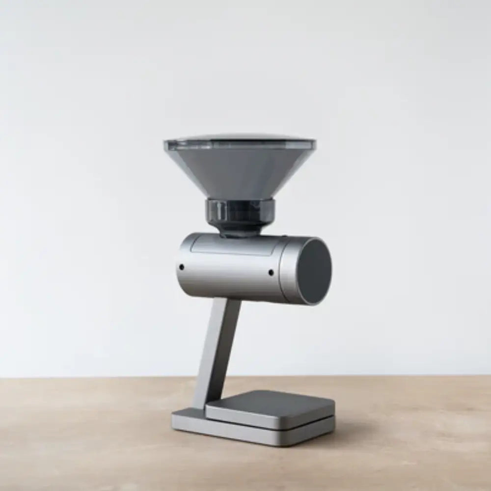 Side view of the Acaia Orion Nano coffee bean doser in grey with a transparent hopper on a wooden surface.