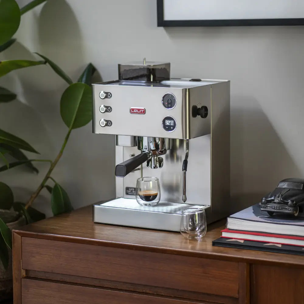 A Lelit Kate espresso machine brewing a shot of espresso into a glass on a countertop.