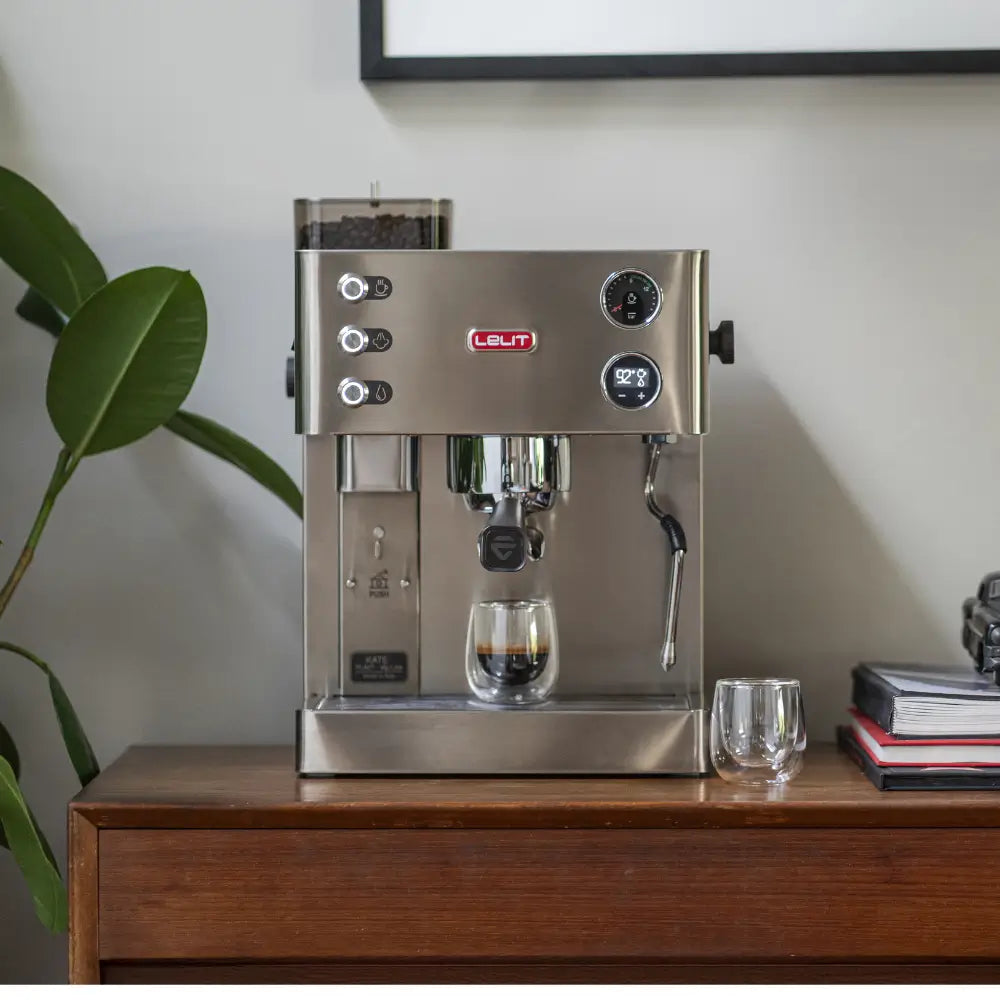 A Lelit Kate espresso machine brewing a shot of espresso into a glass on a countertop.