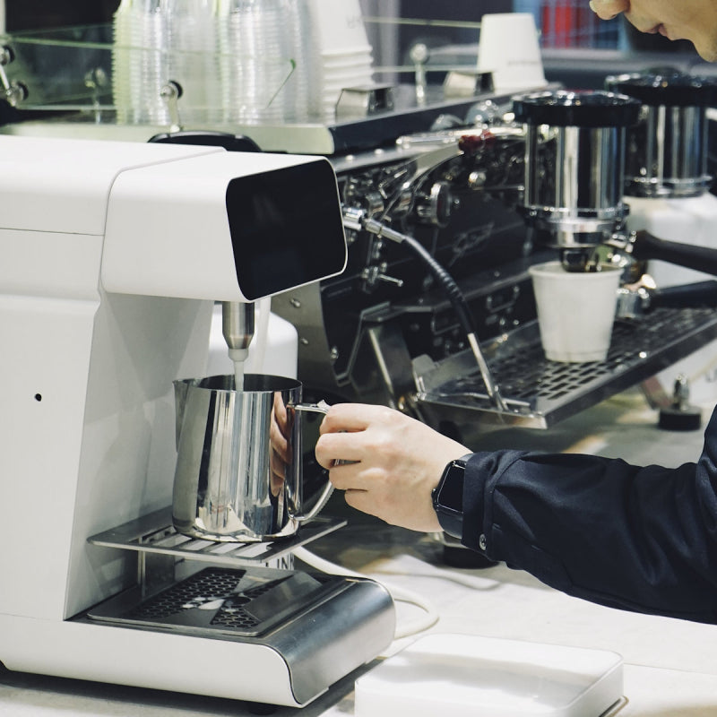 Close-up of Marco MilkPal steamless milk dispenser frothing milk into a stainless steel pitcher