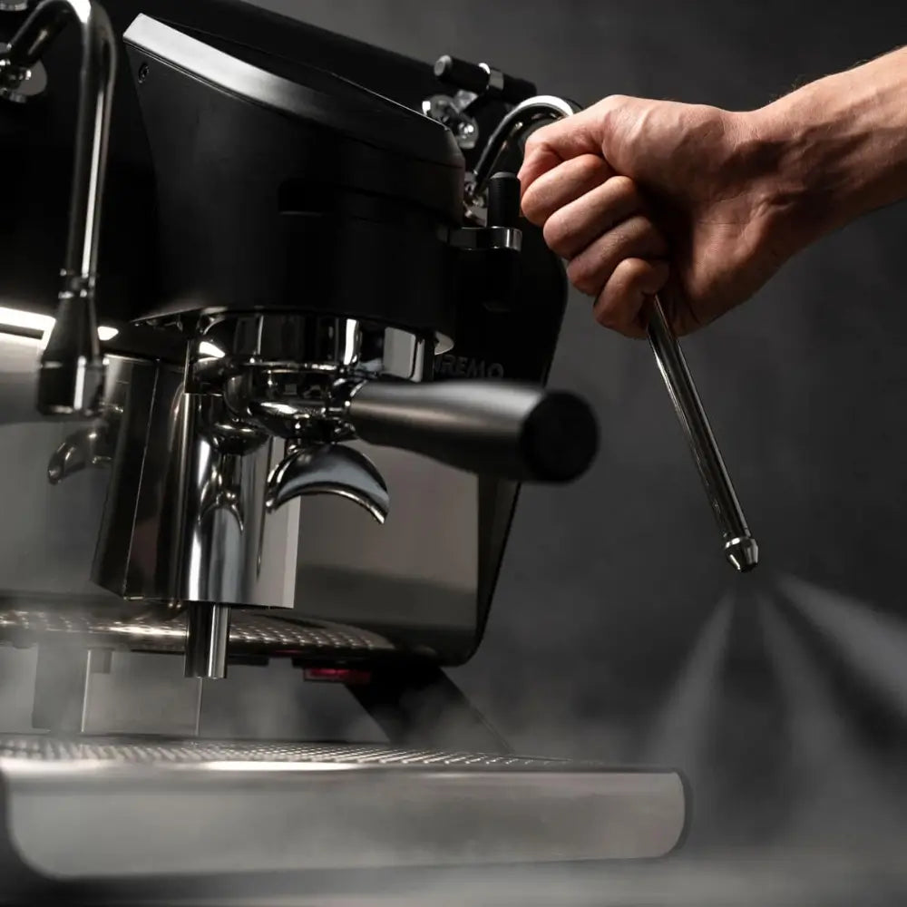 A hand operating the lever for the professional steam wand on the Sanremo YOU, releasing powerful steam for frothing.
