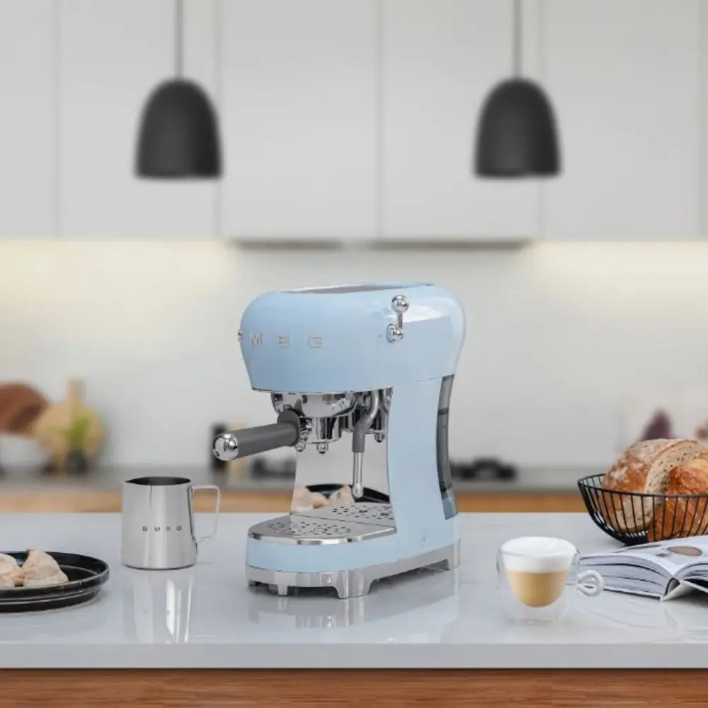 SMEG ECF02 espresso machine in a pastel blue finish on a white kitchen island, next to a freshly made latte.