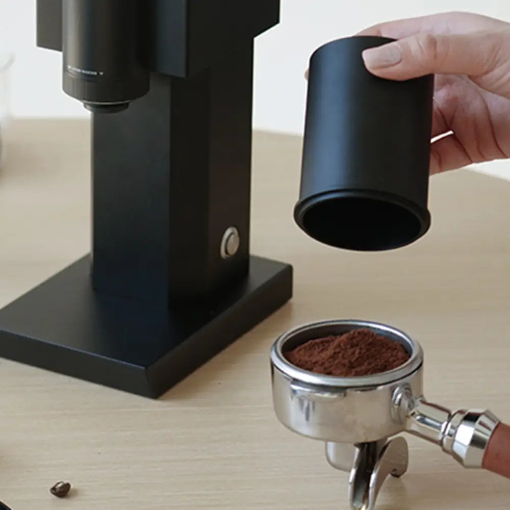 Pouring freshly ground coffee from the Timemore Bricks 01S catch cup into an espresso portafilter, illustrating the grinder's suitability for espresso workflow.