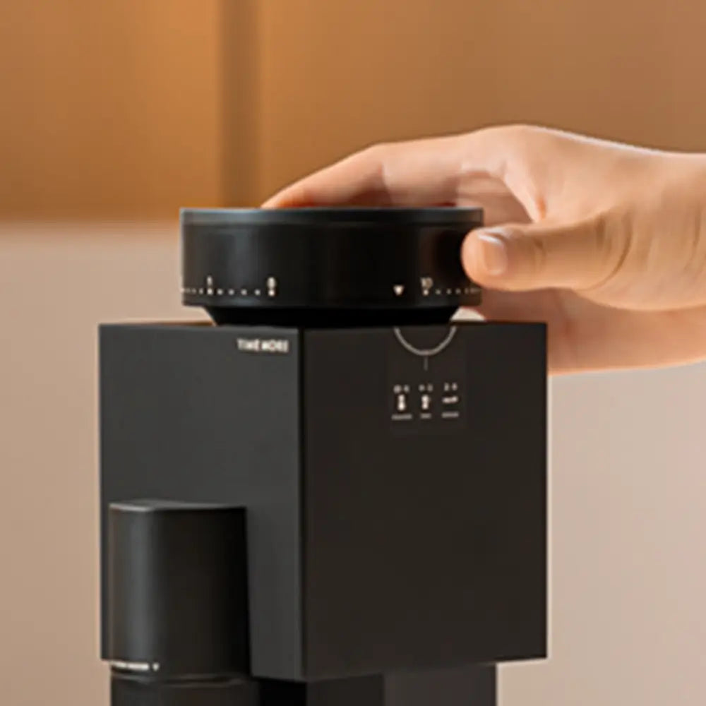 A user's hand adjusting the large, numbered grind size dial on top of the Timemore Bricks 01S, demonstrating precise stepped adjustment for different brew methods.