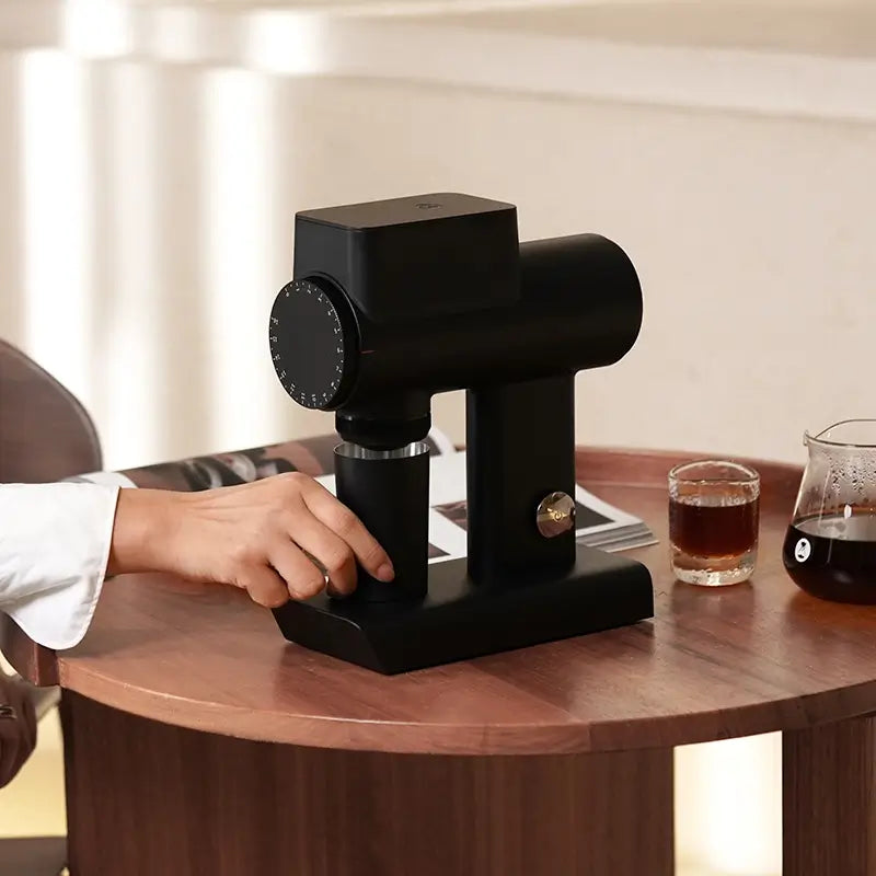 Black Timemore Sculptor 064S coffee grinder on wooden table with coffee cups.