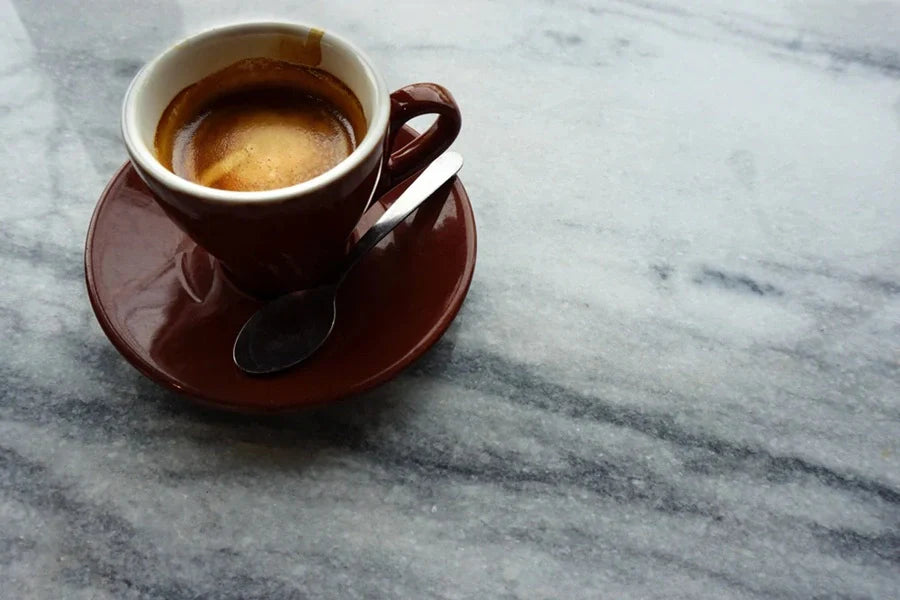 Brown coffee cup and saucer with a spoon and freshly poured espresso shot.