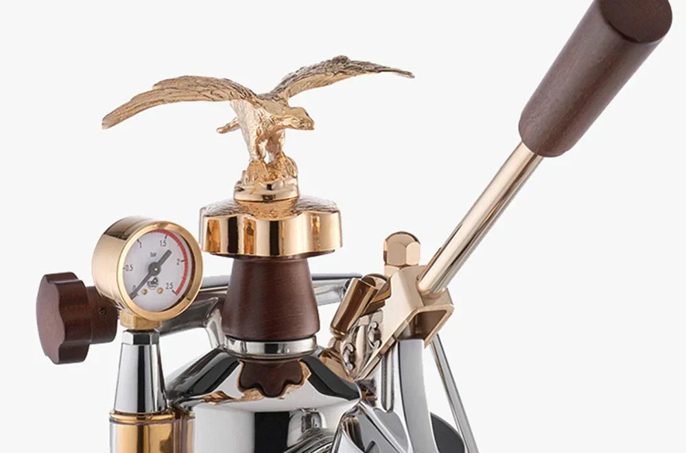 Close-up detail of the La Pavoni manual lever espresso machine featuring the iconic gold eagle topper, wooden handles, and chrome finish with gold accents.
