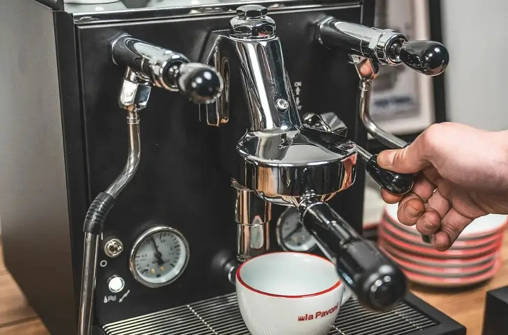 Close-up of a home barista operating the E61 group head lever on a matte black La Pavoni Cellini Evolution semi-professional espresso machine.