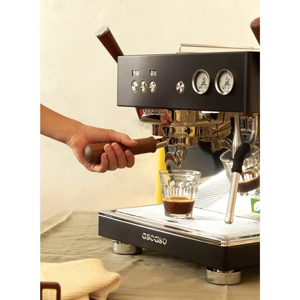 Close-up of a hand inserting the portafilter into the Ascaso Baby T Plus espresso machine during coffee preparation.