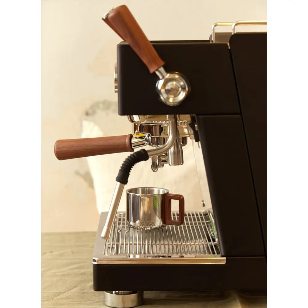 Side angle of the Ascaso Baby T Plus featuring steam wand and portafilter in use, with a metal cup on the drip tray.