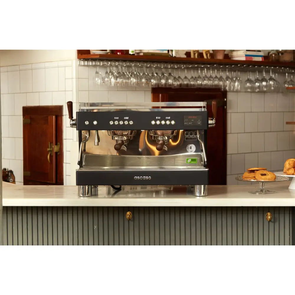 Front view of the Ascaso Barista T Pro 2 Group espresso machine on a café counter, with pastries and glassware in the background.