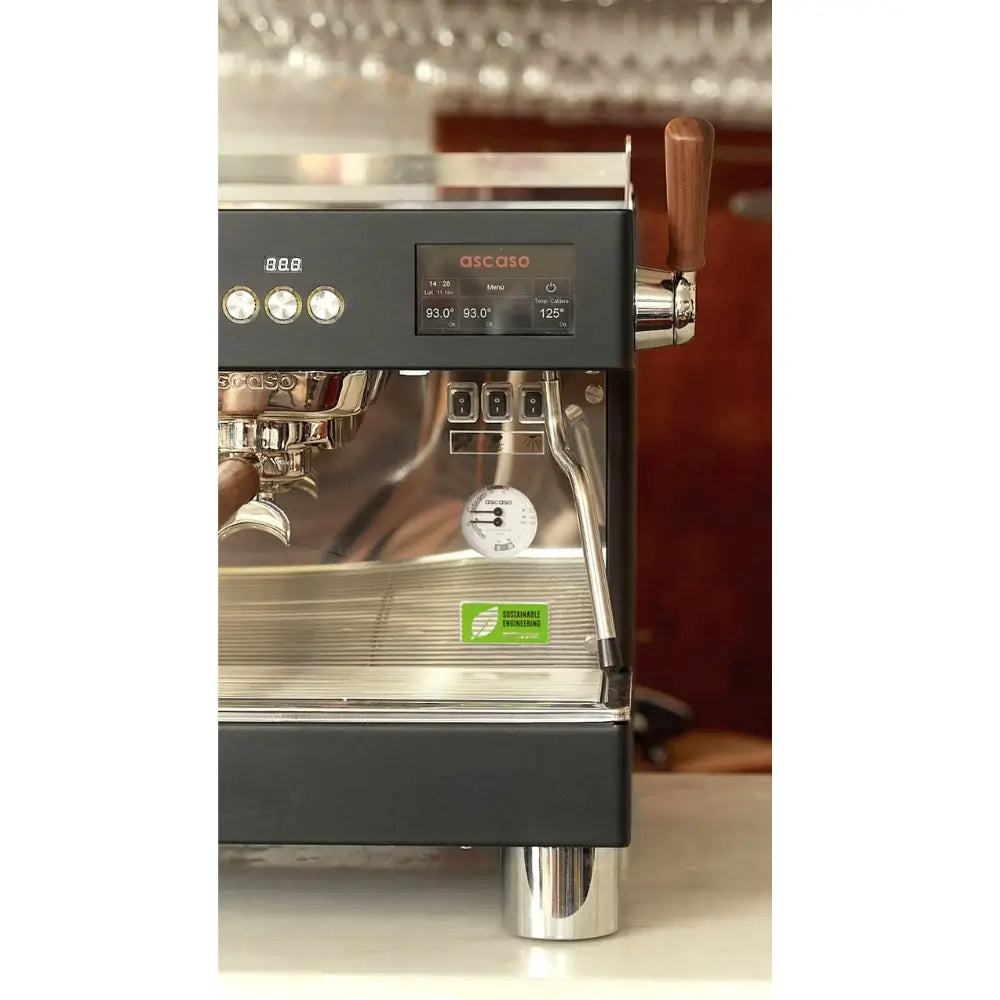 Close-up of the Ascaso Barista T Pro 2 Group espresso machine showing digital control panel, steam wand, and temperature display on a bar countertop.
