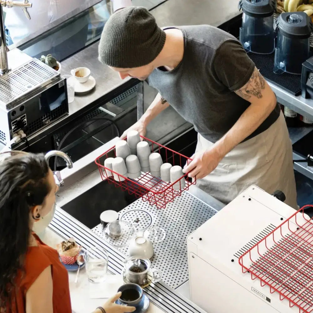 High-angle shot of a barista collecting clean coffee cups while a customer waits at the service counter.