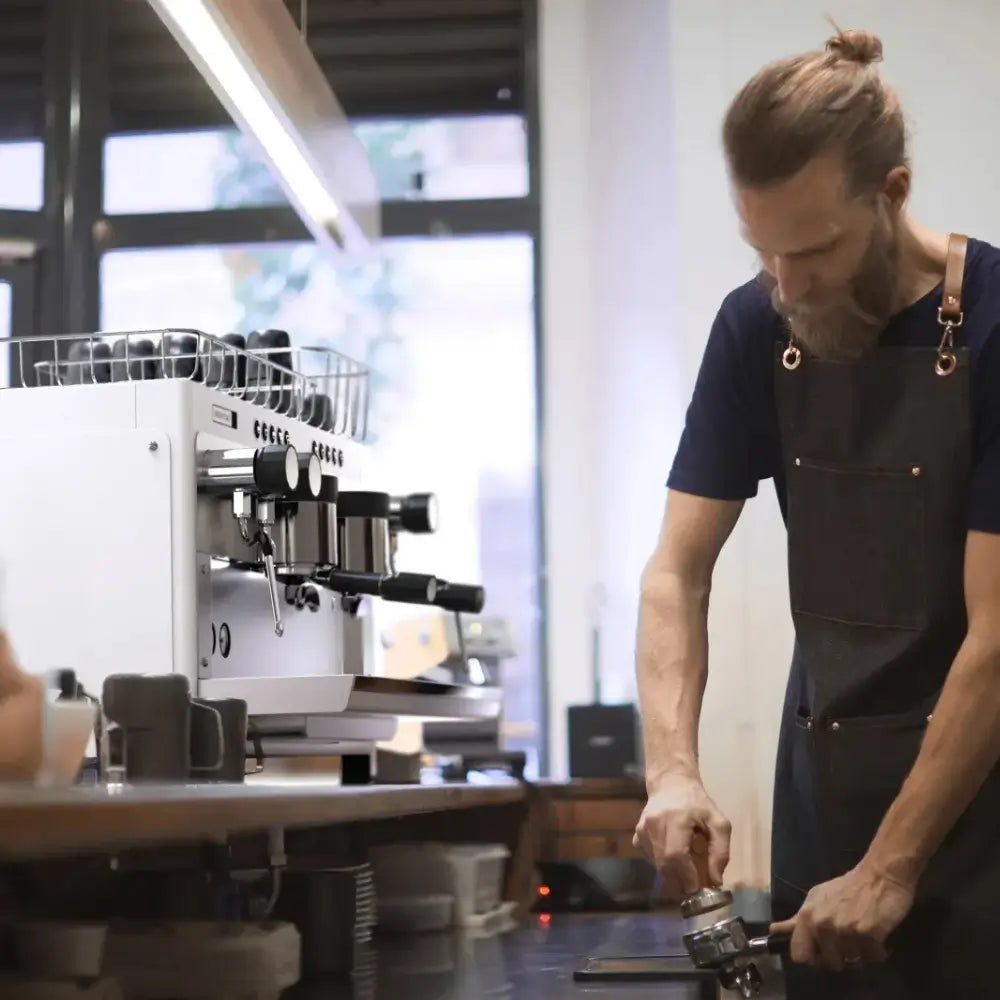 Barista next to the large Iberital Tandem espresso machine in a bright cafe setting.