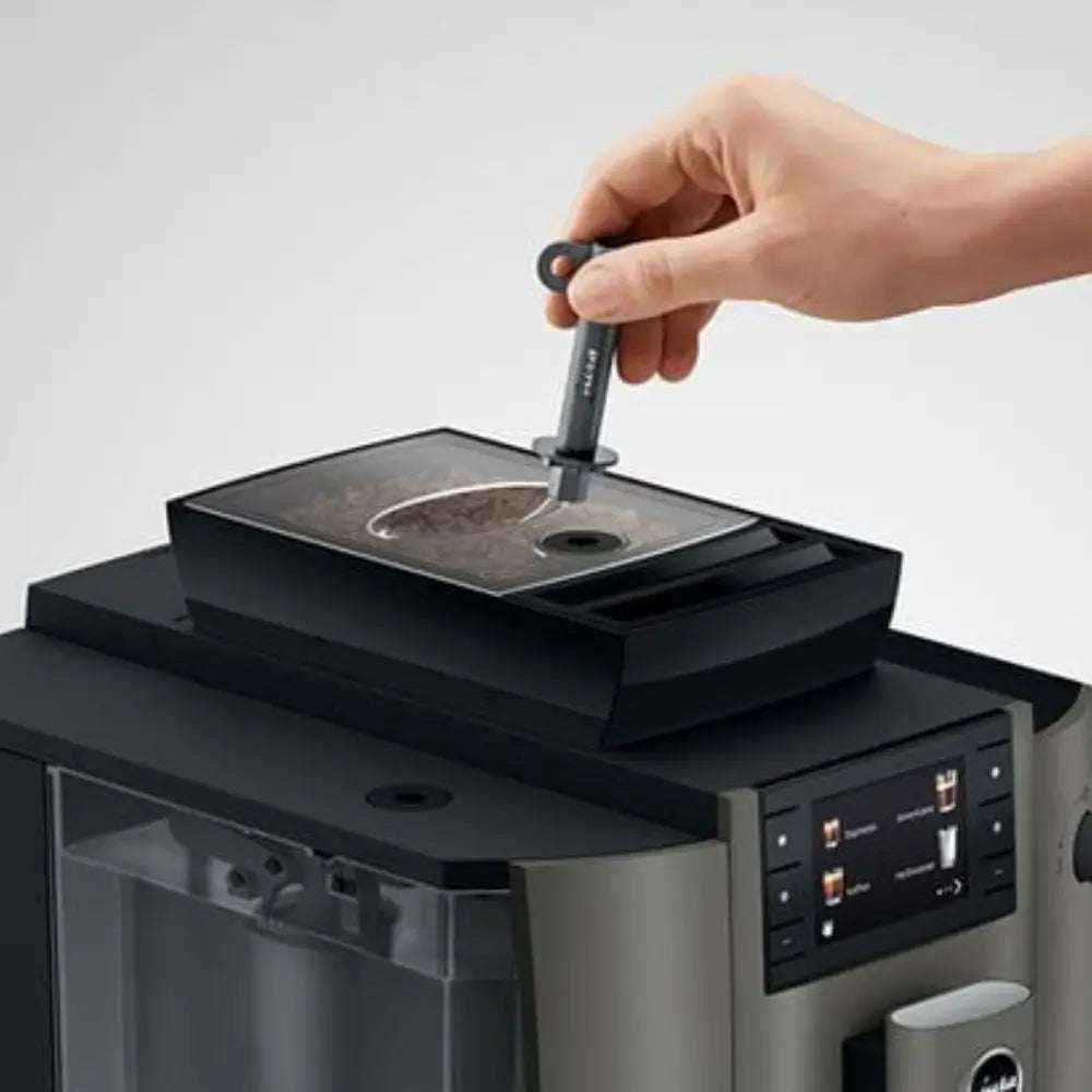 Hand pouring fresh coffee beans into the Jura W4 bean-to-cup machine hopper.