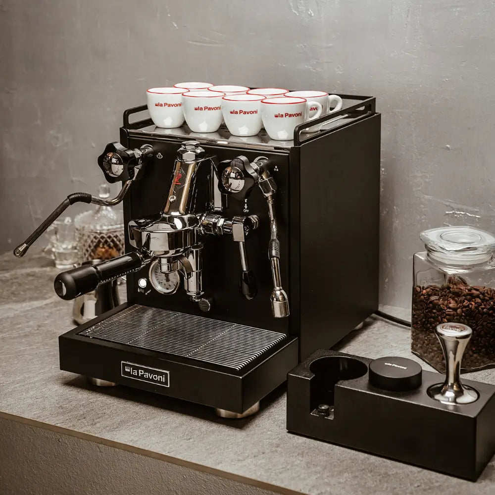 Black La Pavoni Cellini Classic machine on a countertop with cups, tamper, and accessories.