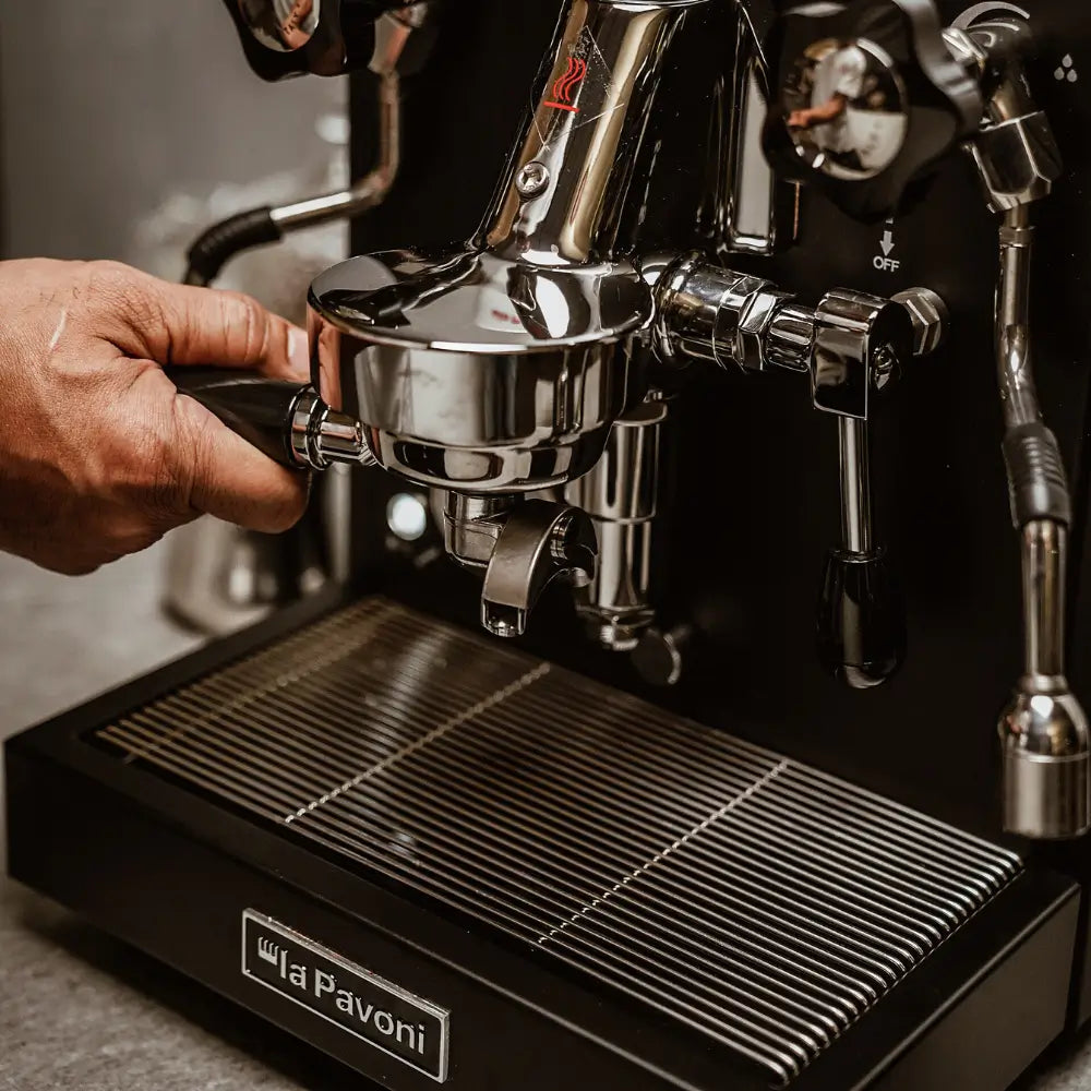 A hand locking the portafilter into the group head of the black La Pavoni Cellini Classic espresso machine.