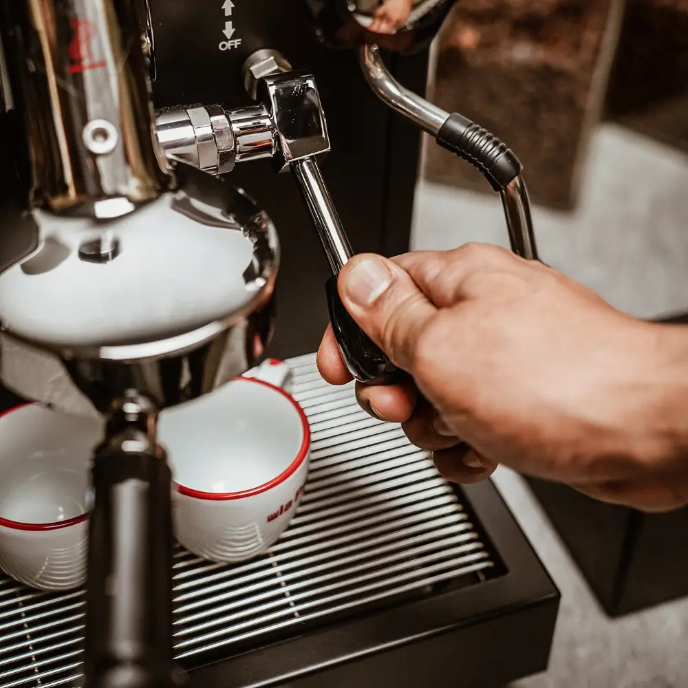 A hand operating the chrome steam valve on the black La Pavoni Cellini Classic espresso machine.