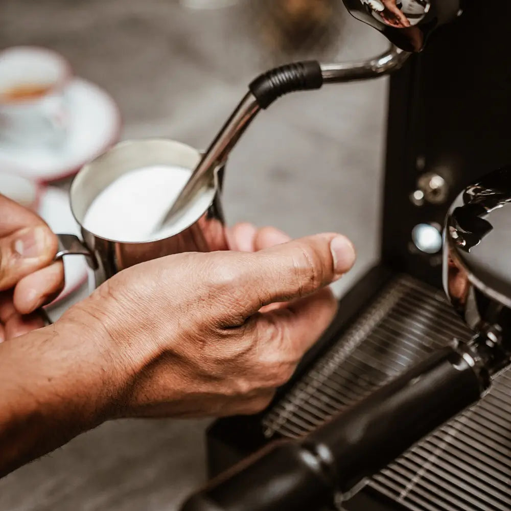 A hand using the steam wand to froth milk in a stainless steel jug on the La Pavoni Cellini Classic.