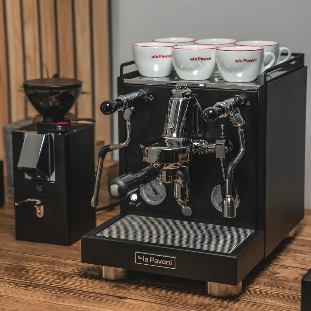 Black La Pavoni Cellini Evolution machine and matching grinder on a wooden countertop coffee setup.