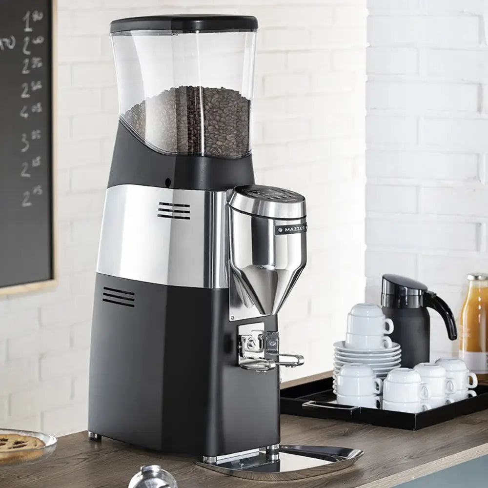 A Mazzer Kold S Electronic coffee grinder filled with beans, set up on a counter in a professional cafe environment.