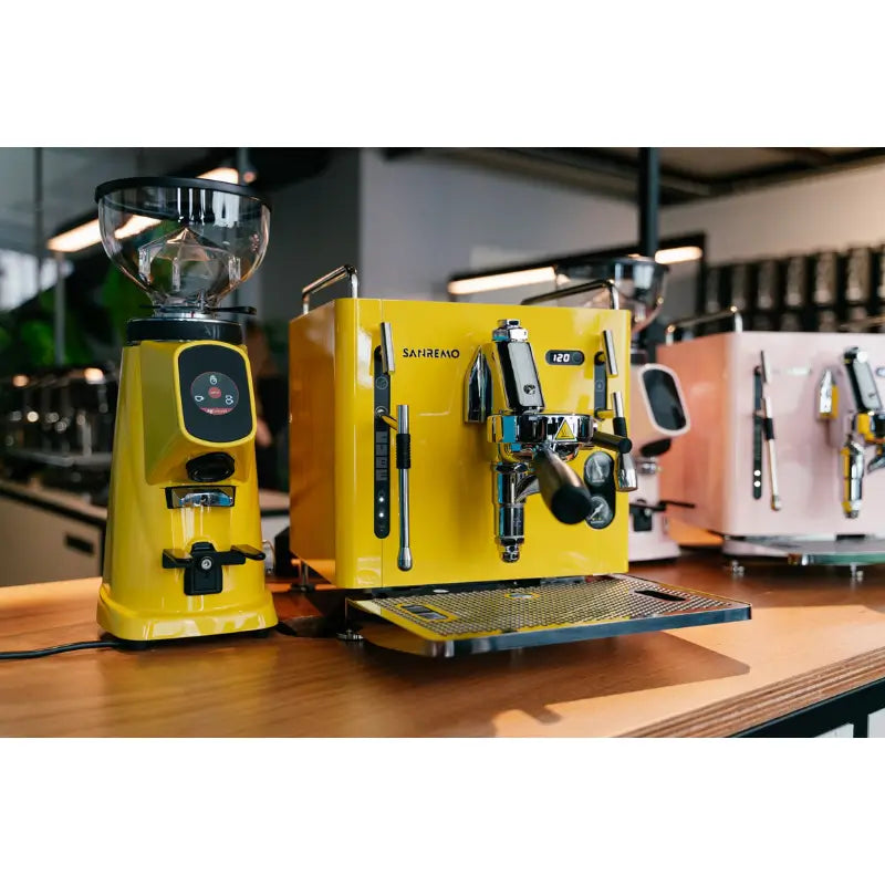 Lifestyle shot of the yellow Sanremo Cube R espresso machine paired with a matching commercial grinder on a wooden bar.