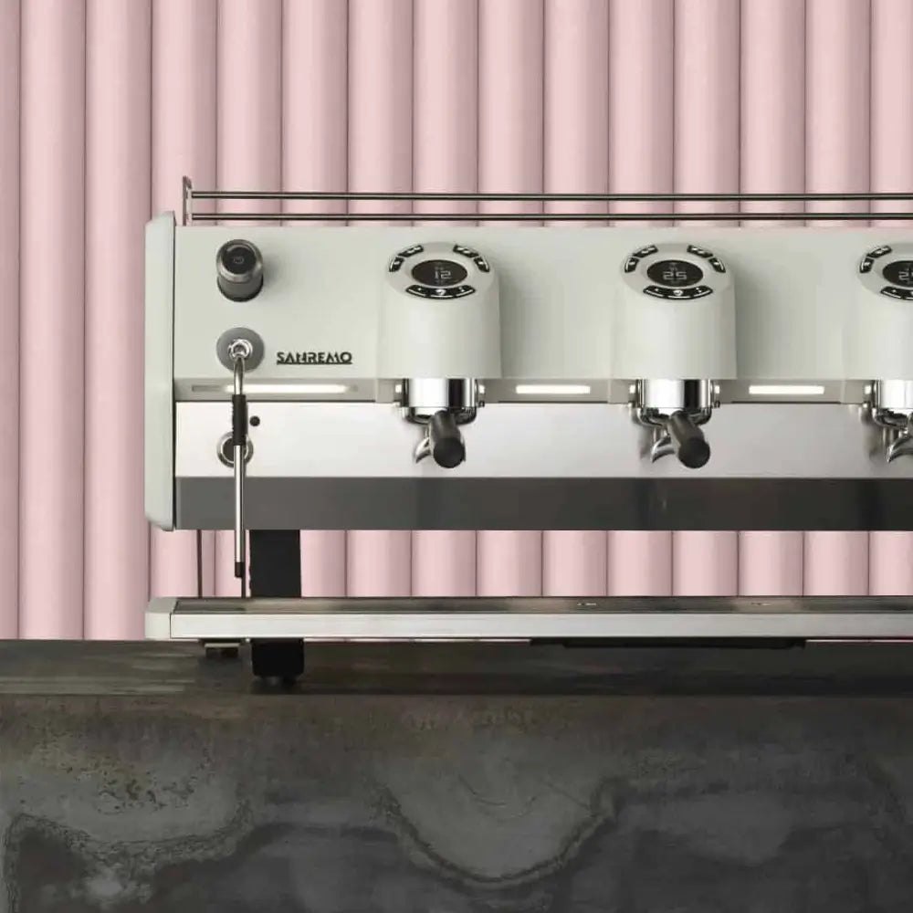 Lifestyle shot of the Sanremo D8 Pro 3-group machine in white, showing digital group heads against a modern pink background.