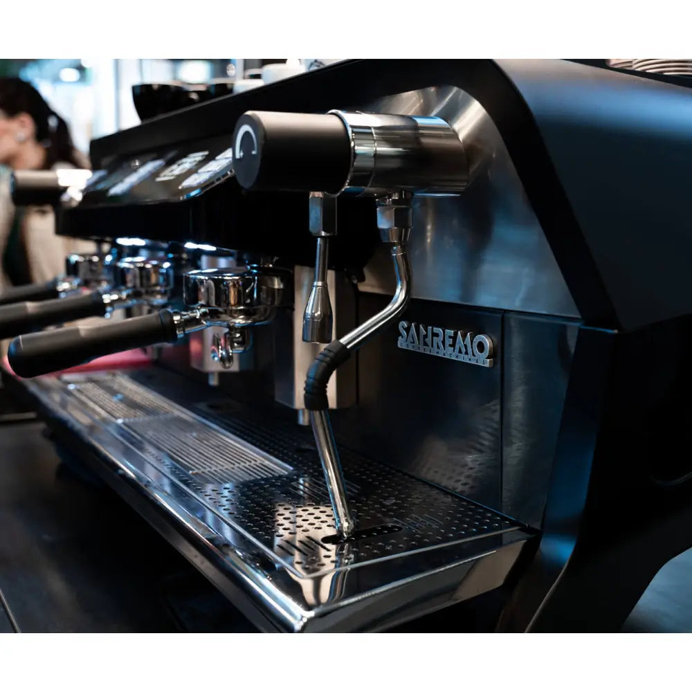 Side angled view of the Sanremo F18 Multi Boiler on a commercial coffee bar, demonstrating its sleek profile and cup-warming rail