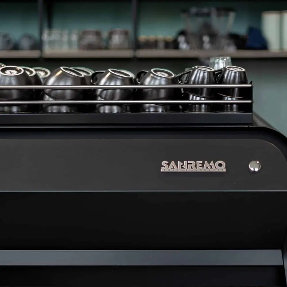 Close-up of the Sanremo logo and the cup warming tray on the top of the F18 Multi Boiler machine.