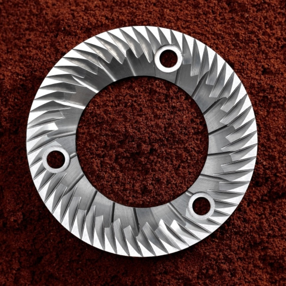 Extreme close-up of the professional 64mm flat steel burrs of the Sanremo SR64 EVO grinder, lying on a bed of ground coffee.