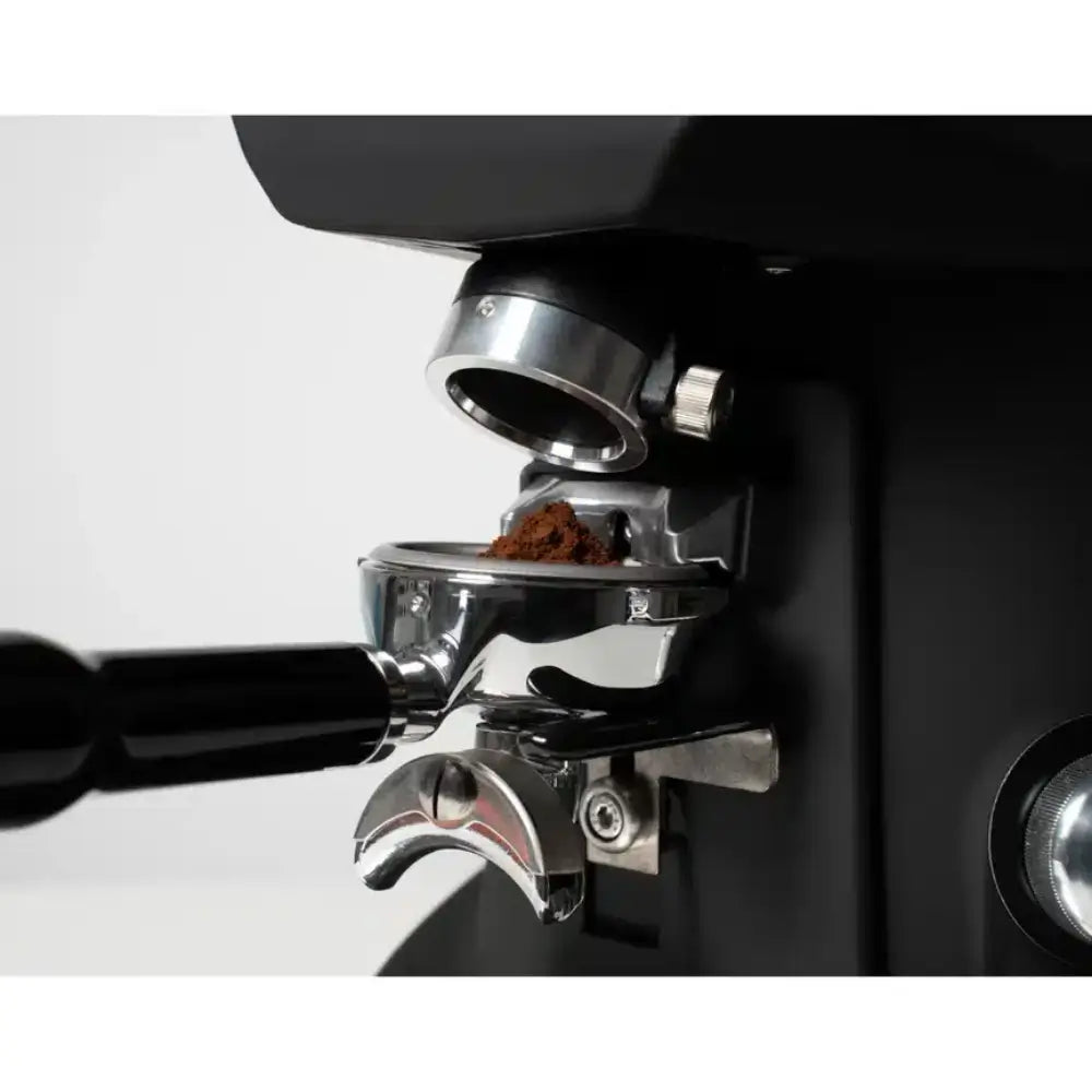 Close-up of the Sanremo SR64 EVO Pro Sense dispensing chute and adjustable portafilter rest with a small amount of ground coffee.