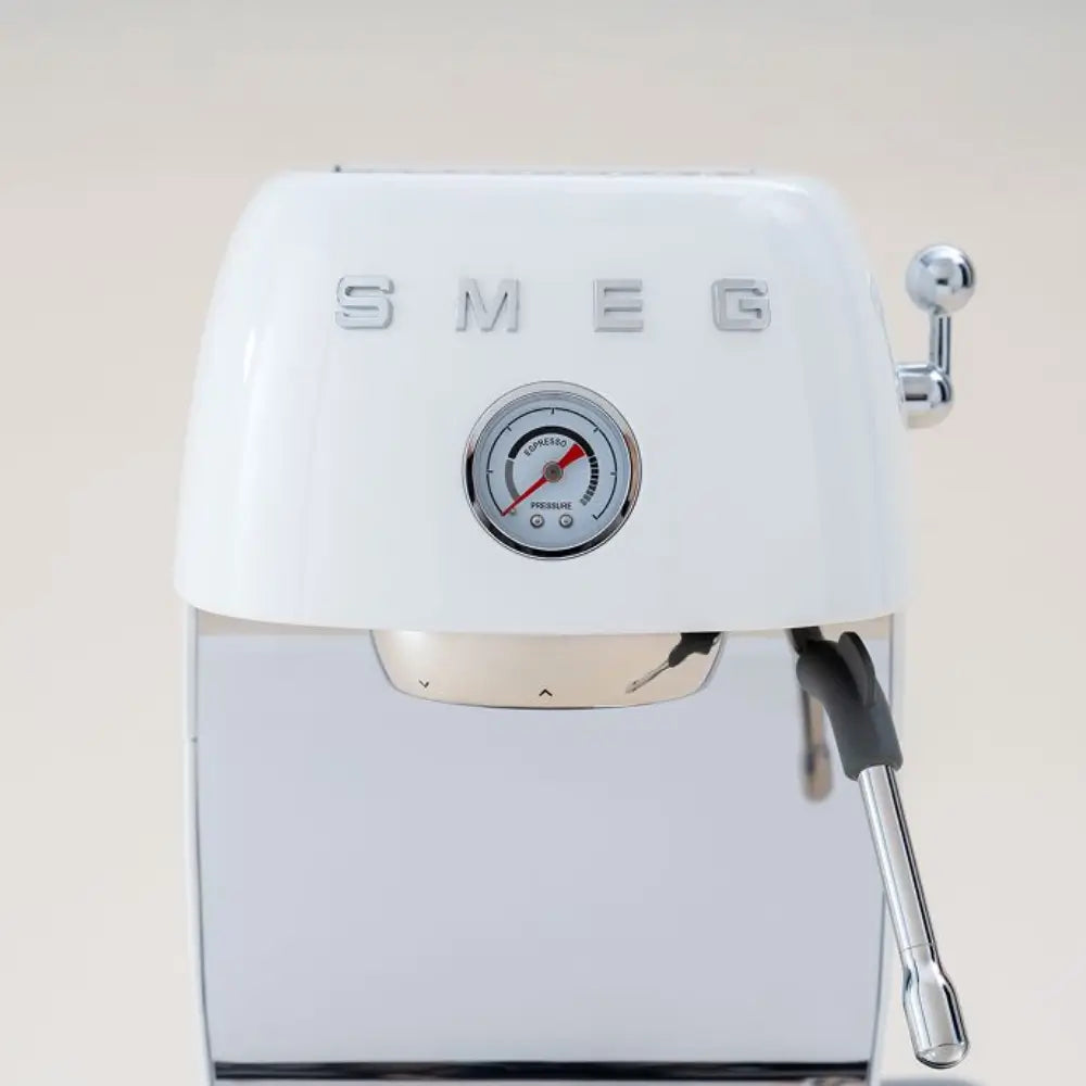 Head-on, close-up detail of the white SMEG ECF03 retro espresso machine highlighting the pressure gauge and steam wand.