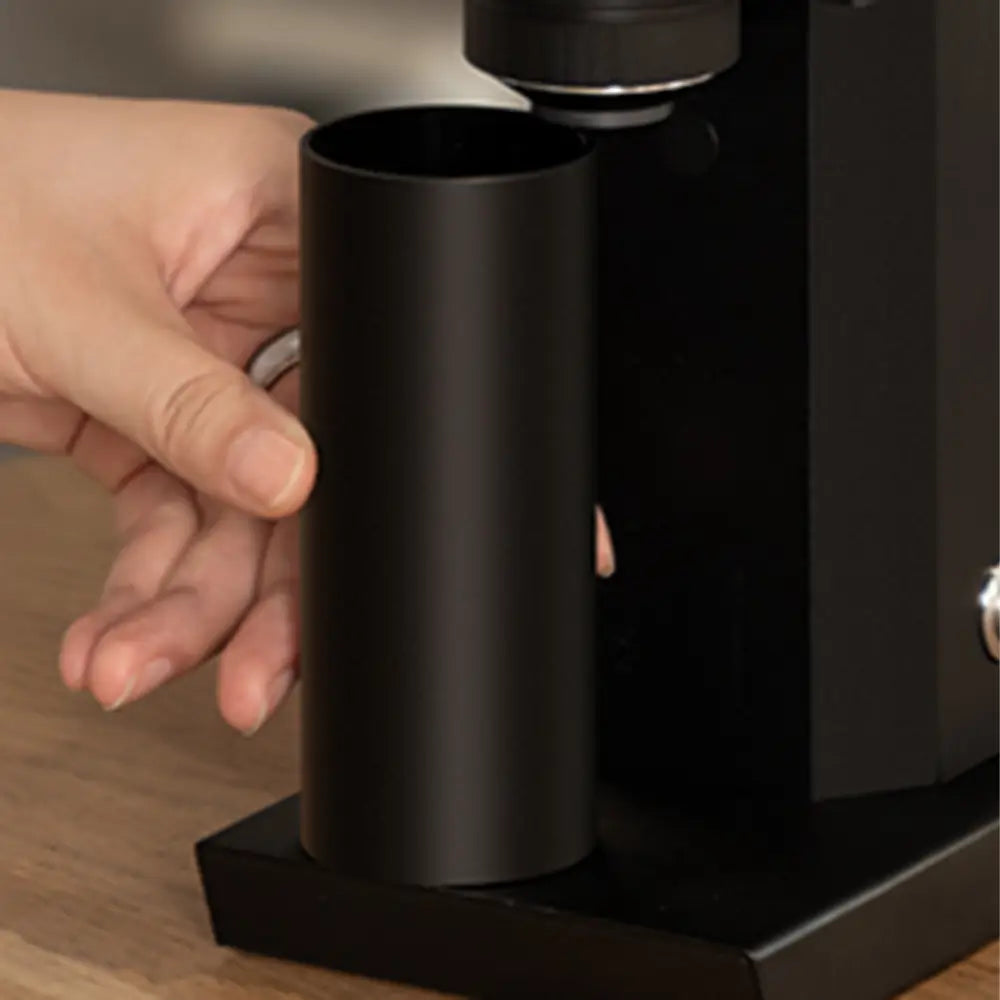 Close-up of a user removing the magnetic catch cup from the black Timemore Bricks 01S grinder, highlighting the vertical chute and easy-access bin.