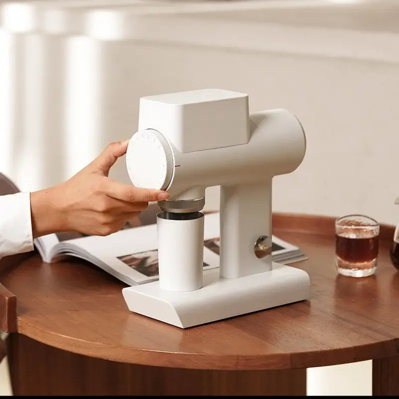 White Timemore Sculptor 064S coffee grinder on table with glass of coffee.