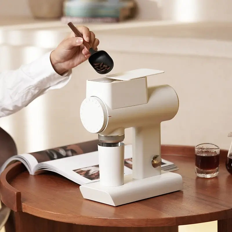 Hand scooping coffee beans into hopper of white Timemore Sculptor 064S grinder.