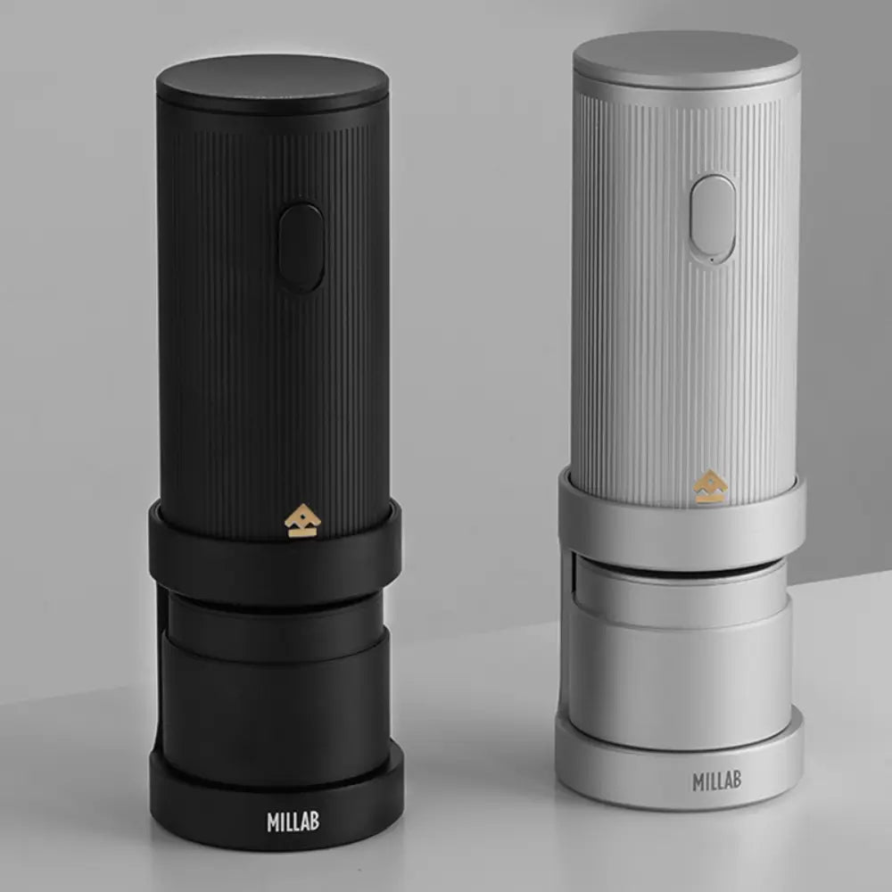 Two Timemore x Millab wireless electric coffee grinders standing side-by-side on a white surface, displaying the matte black and brushed silver color options with their respective charging stands.