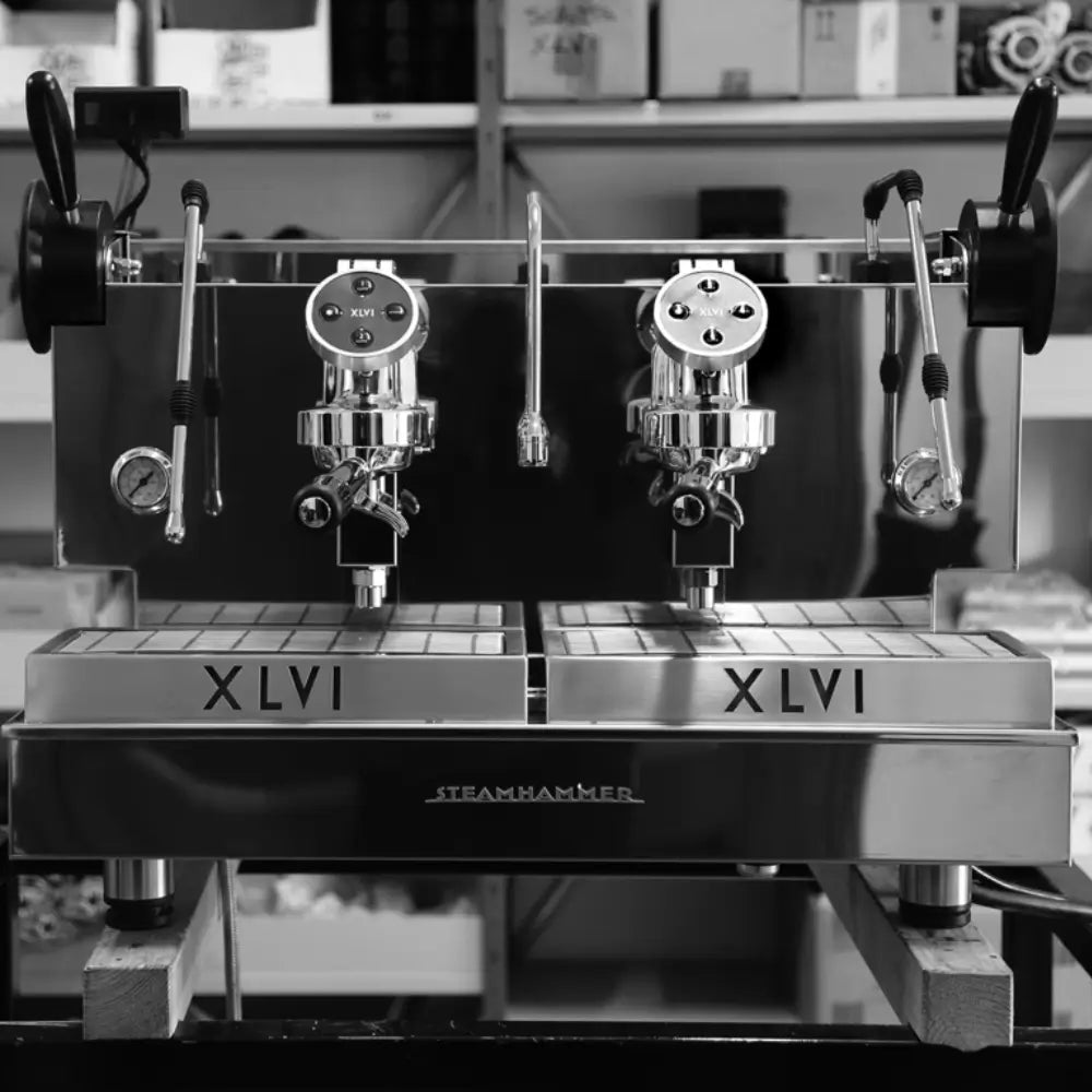 Black and white photo of the XLVI Steamhammer industrial-style 2 Group espresso machine with prominent 'XLVI' branding.