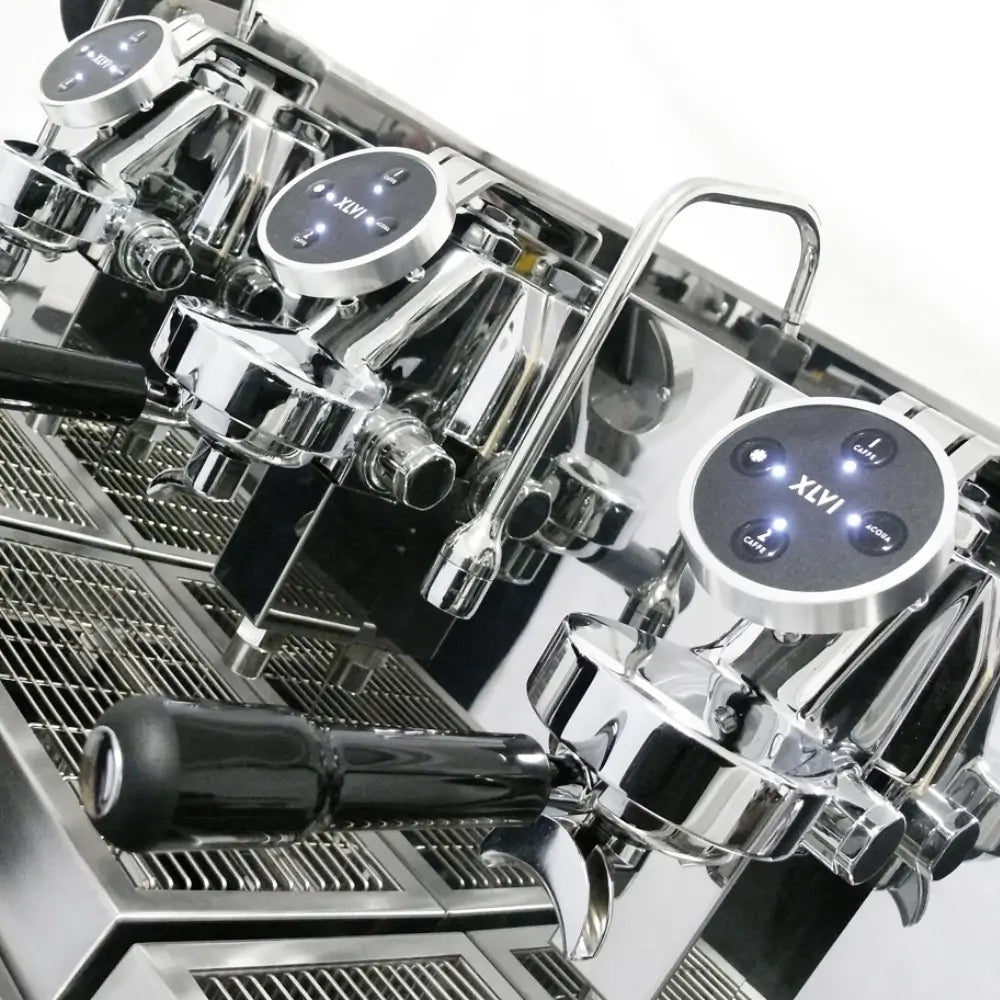 Close-up, angled view of the XLVI Steamhammer E group heads, showing the backlit volumetric control buttons and drip tray.